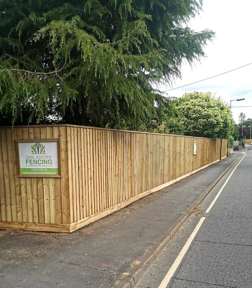 A long roadside close-board fence with the Carl Adcock Fencing sign